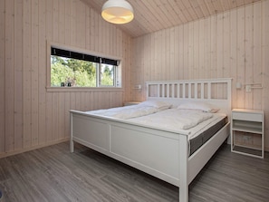 A bedroom with a wooden paneled wall, a bed with a white headboard, a bedside table, and a window with blinds. - 5 Star Holiday Home in Vaeggerlose (Vaeggerlose)