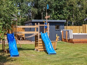 A wooden play structure with two slides and a small building with a window.
