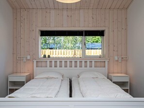 A bedroom with a bed, two bedside tables, a window with a view of a wooden fence, and a ceiling with wooden panels. - 5 Star Holiday Home in Vaeggerlose (Vaeggerlose)