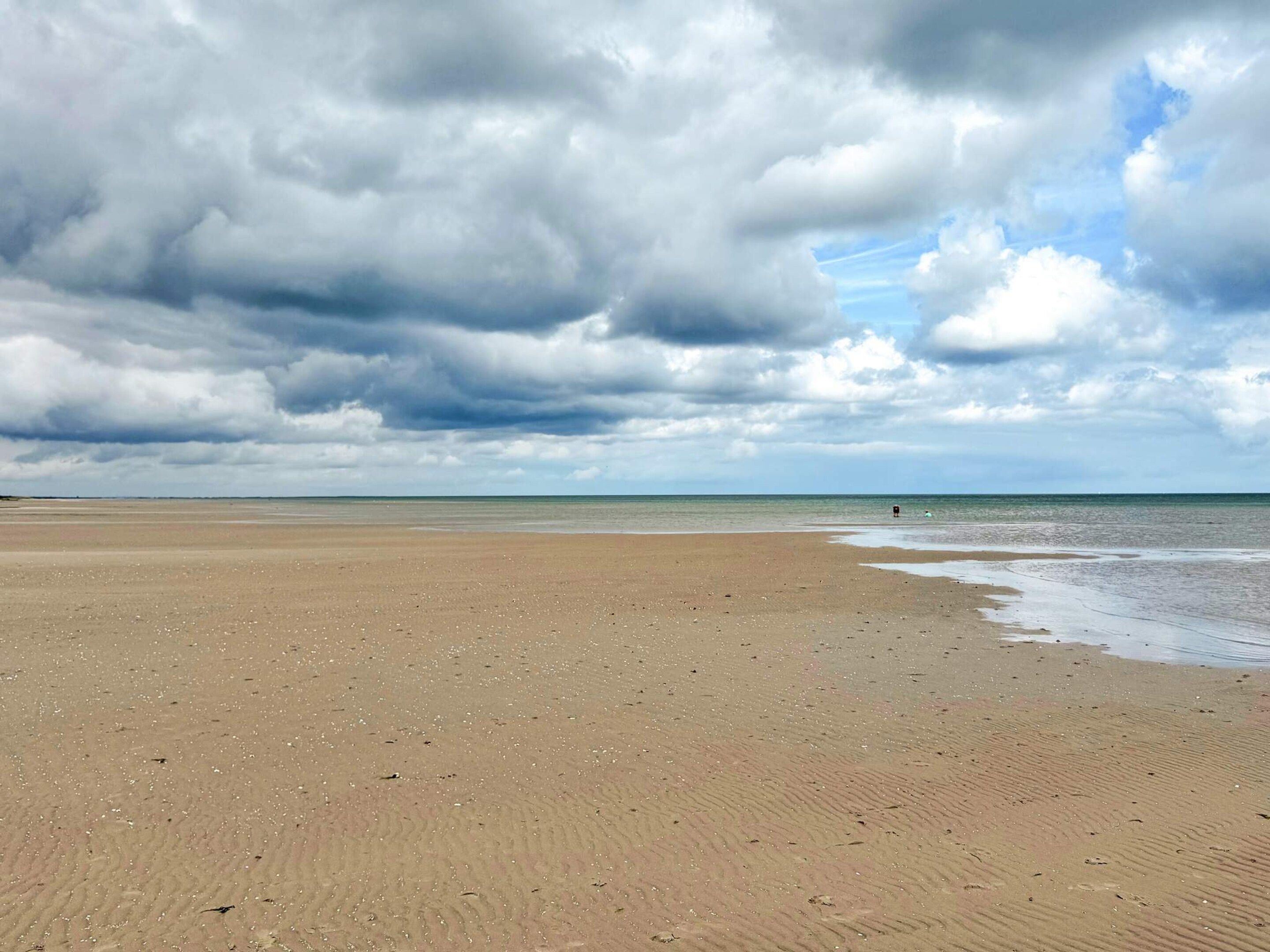 A wide sandy beach with gentle waves, under a partly cloudy sky.