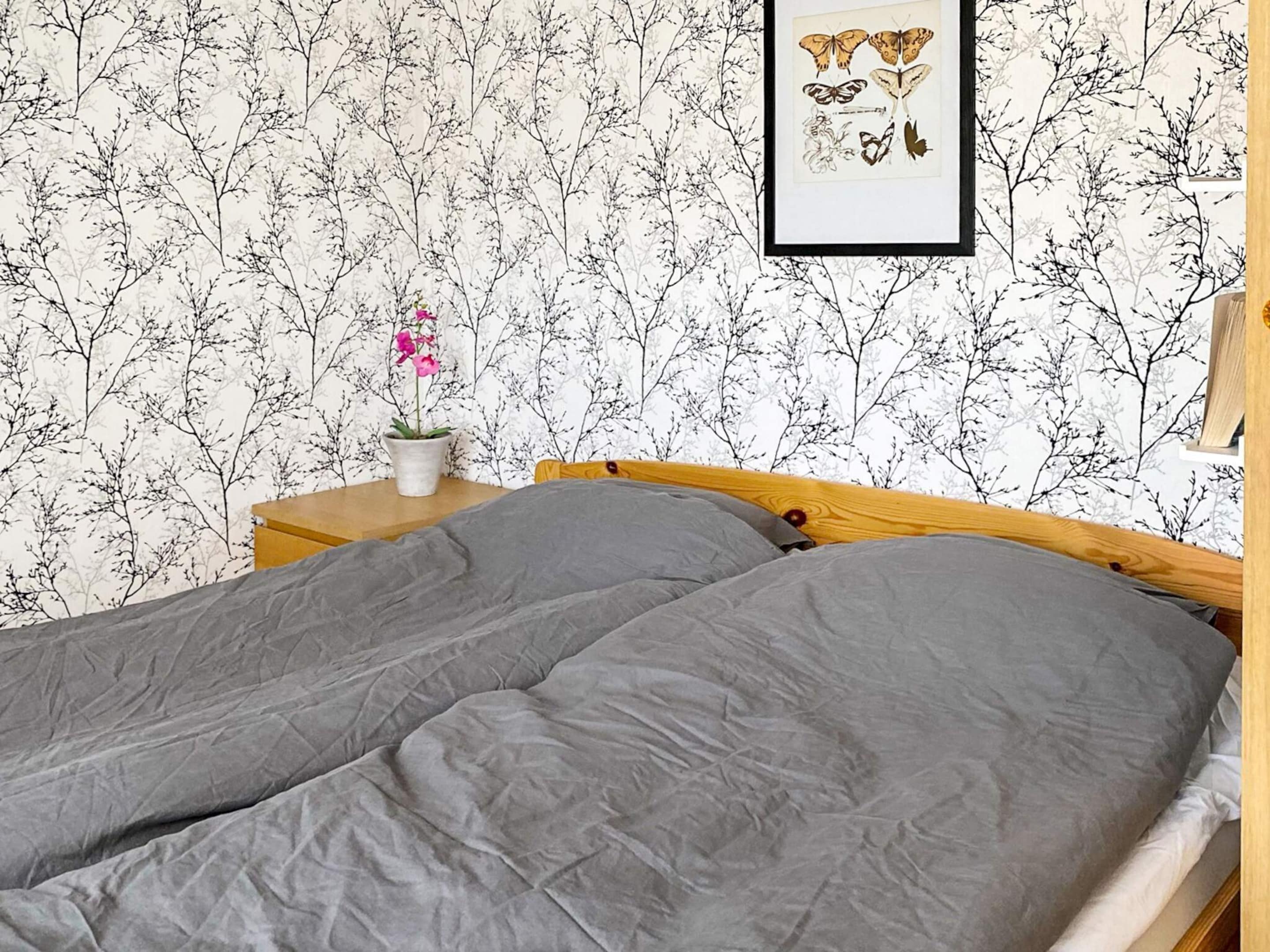 A bedroom with a bed, a nightstand, a potted plant, and a framed picture on the wall.