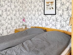 A bedroom with a bed, a nightstand, a potted plant, and a framed picture on the wall.