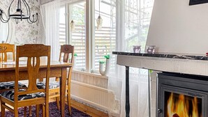 A cozy room with a wooden dining table, chairs, a fireplace, and a window with blinds. - 4 Star Holiday Home in Figeholm (Figeholm)