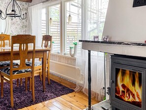 A cozy room with a wooden dining table, chairs, a fireplace, and a window with blinds. - 4 Star Holiday Home in Figeholm (Figeholm)