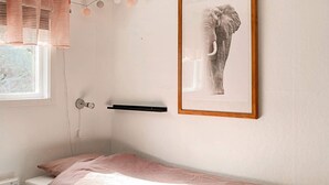 A single bed with a pink mattress and pillow, a bedside table, a framed picture on the wall, and a window with blinds. - 4 Star Holiday Home in Figeholm (Figeholm)