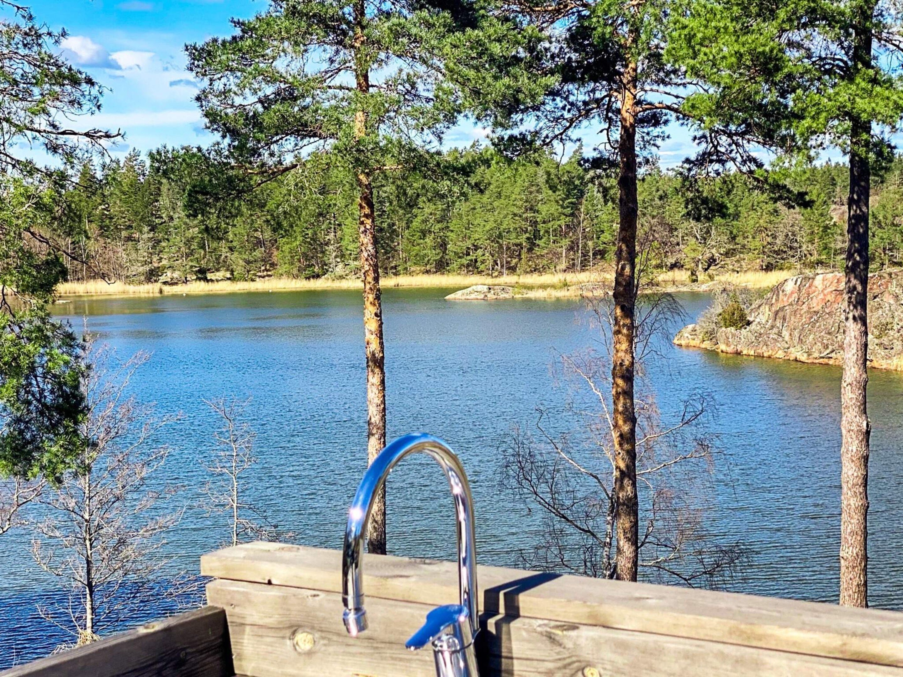 Une terrasse en bois avec un robinet en métal, donnant sur un lac paisible entouré d’arbres.