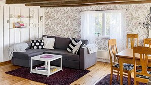A cozy living room with a grey sofa, a small white side table, and a dining area with wooden chairs and a table. - 4 Star Holiday Home in Figeholm (Figeholm)