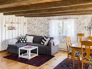 A cozy living room with a grey sofa, a small white side table, and a dining area with wooden chairs and a table. - 4 Star Holiday Home in Figeholm (Figeholm)