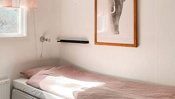Una cama individual con colchón y almohada rosa, una mesita de noche, un cuadro en la pared y una ventana con persianas.