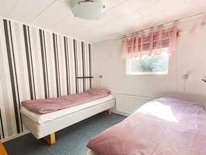 A bedroom with a bunk bed, a single bed, a radiator, a window with curtains, and a striped wall. - 4 Star Holiday Home in Figeholm (Figeholm)