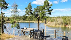 A wooden deck with a table and chairs, overlooking a lake with trees in the background. - 4 Star Holiday Home in Figeholm (Figeholm)