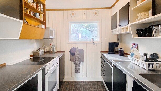 A compact kitchen with a microwave, stove, and a window with a view of greenery. - 4 Star Holiday Home in Figeholm (Figeholm)