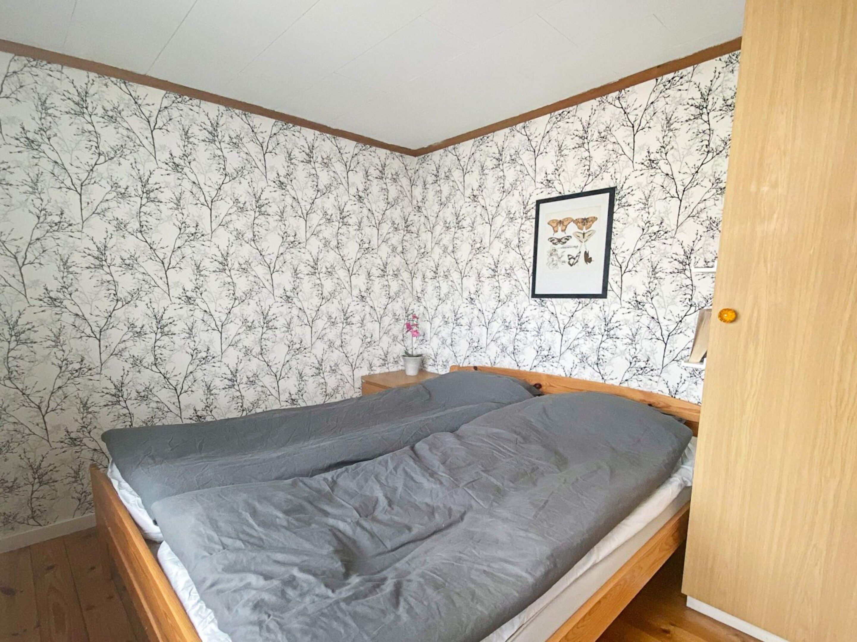 A bedroom with a bed, a nightstand, a framed picture, and a door.