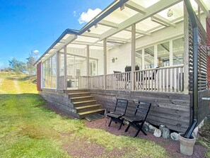 A covered porch with a wooden railing, a set of stairs leading to the entrance, and a seating area with benches. - 4 Star Holiday Home in Figeholm (Figeholm)