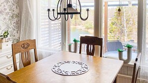 Ruokailutila, jossa on puinen pöytä, tuolit, kattokruunu ja näkymä ulos suurista ikkunoista.