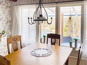 A dining area with a wooden table, chairs, a chandelier, and a view of the outdoors through large windows.