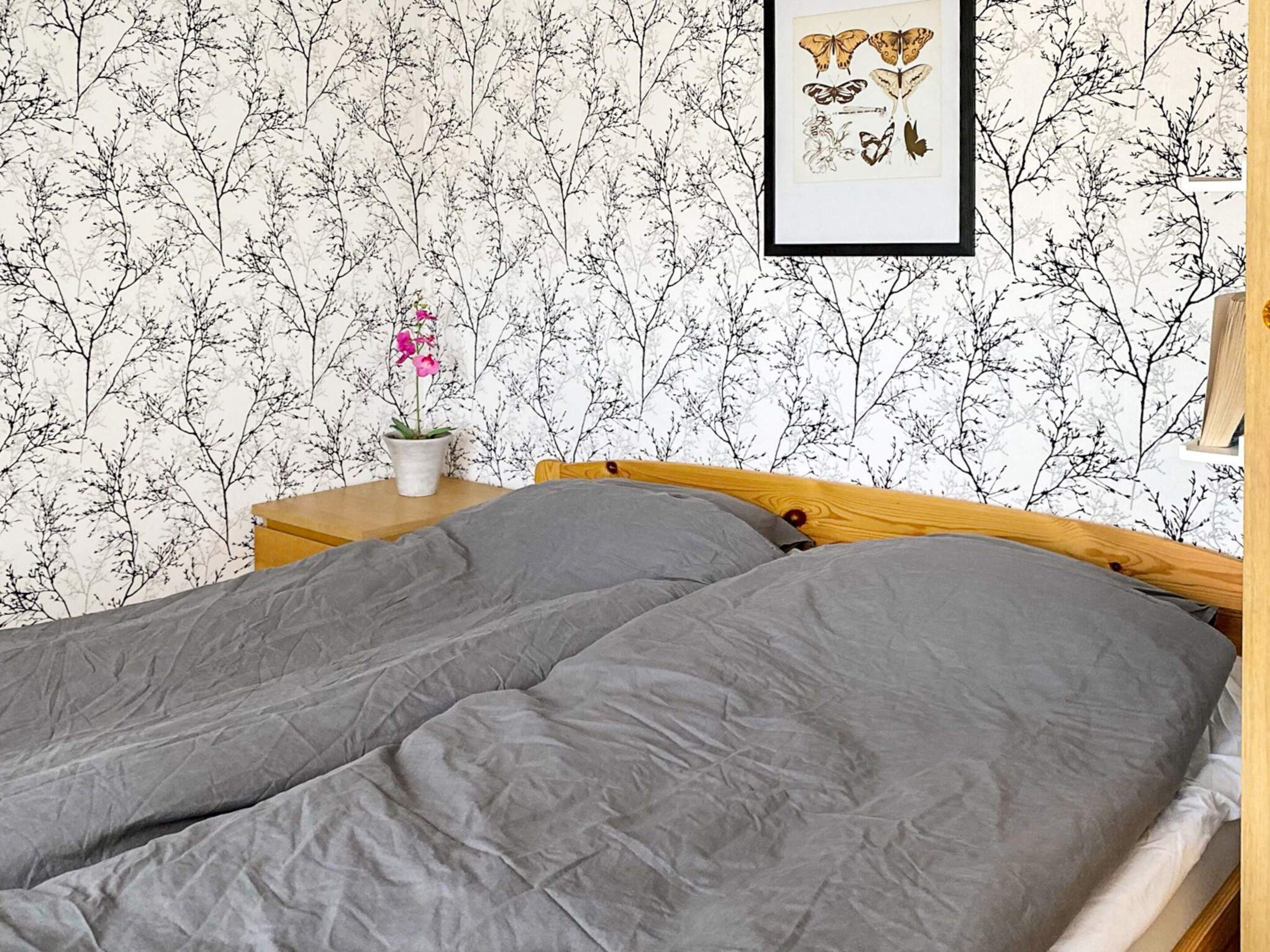 A bedroom with a bed, a nightstand, a potted plant, and a framed picture on the wall.