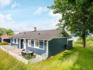 Ett envåningshus med en mörkblå fasad, en vit veranda och en liten uteplats med ett bord och stolar.