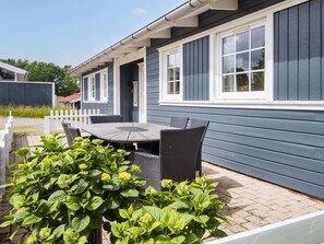 A row of blue mobile homes with a white picket fence, a round table with chairs, and green plants in the foreground. - 4 Star Holiday Home in Aabenraa (Aabenraa)