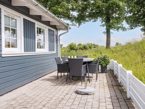 A patio with a table and chairs, a white fence, and a house with dark siding and white trim.