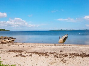 A beach with a wooden pier extending into calm waters, surrounded by rocks and sparse vegetation. - 4 Star Holiday Home in Aabenraa (Aabenraa)