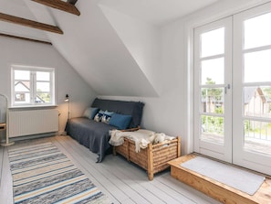 A loft bedroom with a sloped ceiling, a bed with blue pillows, a wicker basket, and a view through a large door.