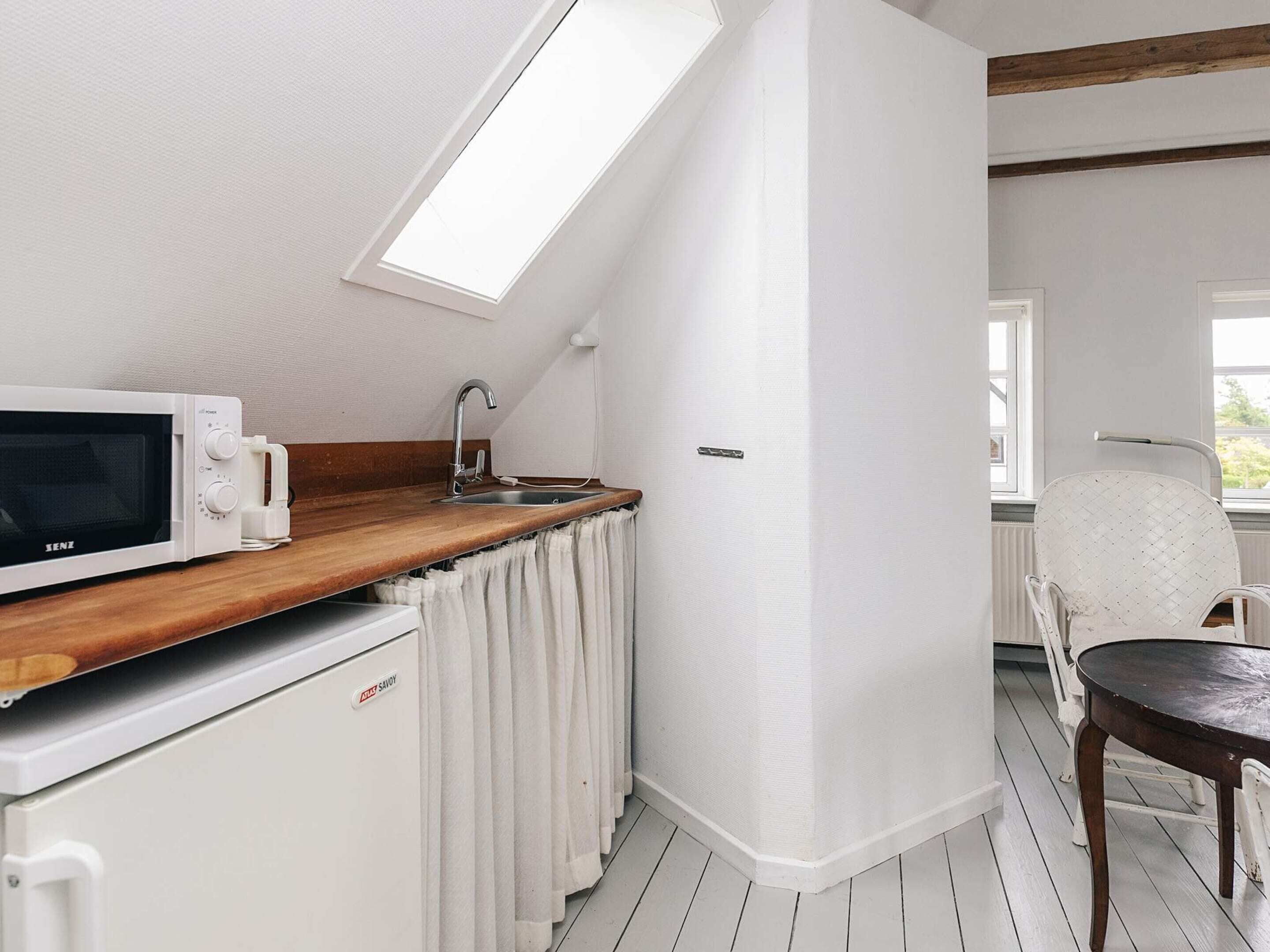 A compact kitchen with a microwave, sink, and wooden countertop.