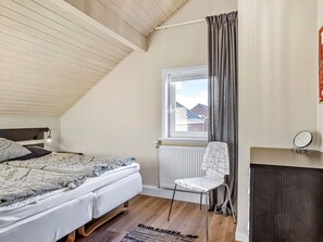 A bedroom with a sloped ceiling, a bed with patterned bedding, a chair, a window with curtains, and a radiator.