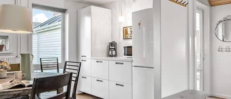 A compact kitchen with white cabinetry, a coffee machine, and a refrigerator.