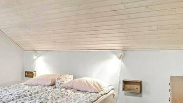 A bedroom with a wooden ceiling, a bed with floral bedding, two bedside tables, and a wall-mounted shelf.