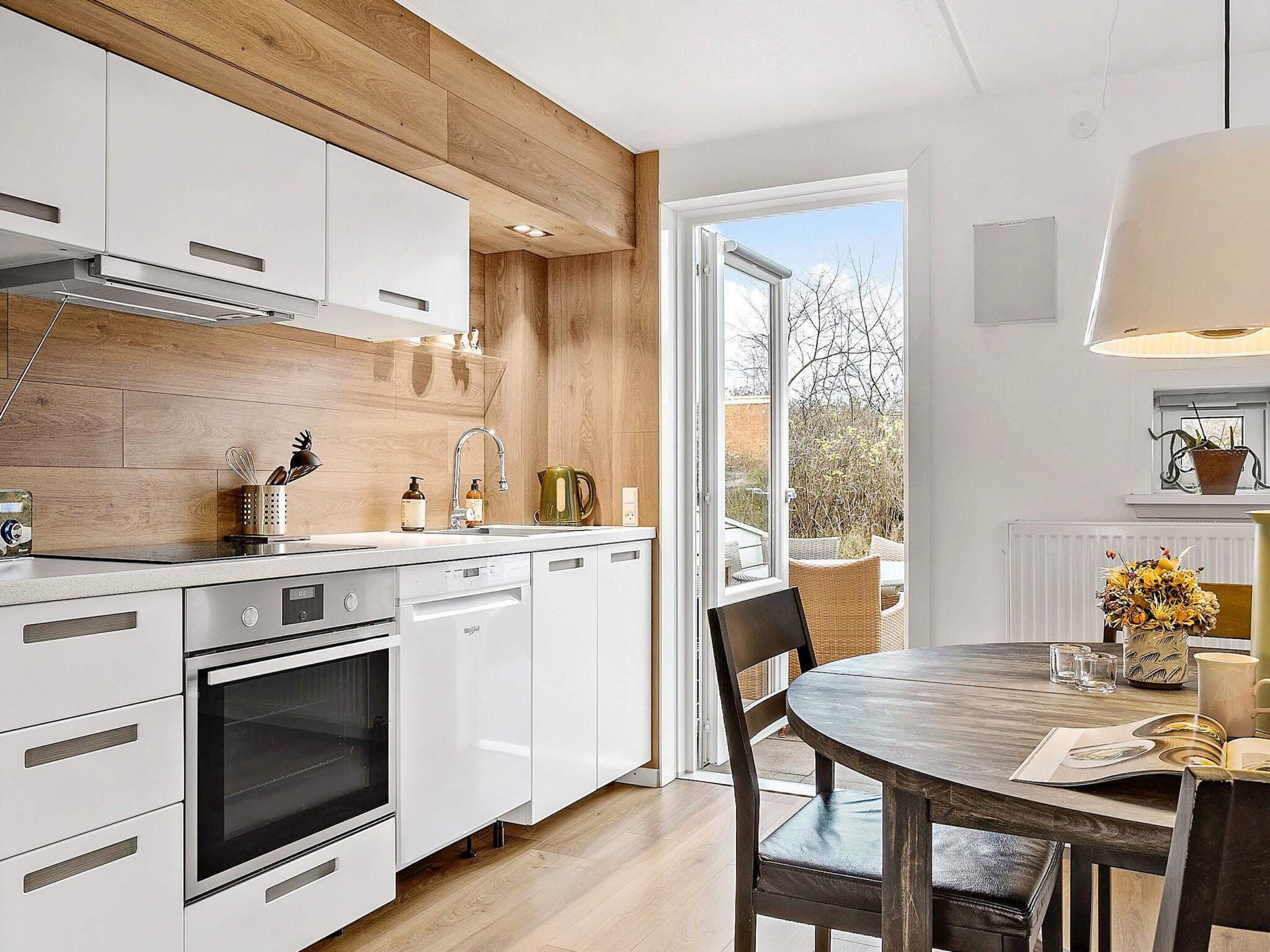 A modern kitchen with white cabinets, a built-in oven, and a dining area with a round table and chairs.