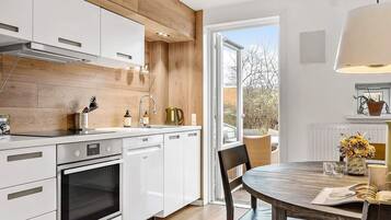 A modern kitchen with white cabinets, a built-in oven, and a dining area with a round table and chairs.