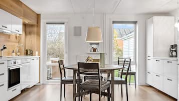 A modern kitchen with white cabinets, a wooden ceiling, and a dining area with a table and chairs.