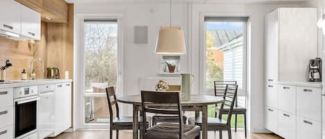 A modern kitchen with white cabinets, a wooden ceiling, and a dining area with a table and chairs.