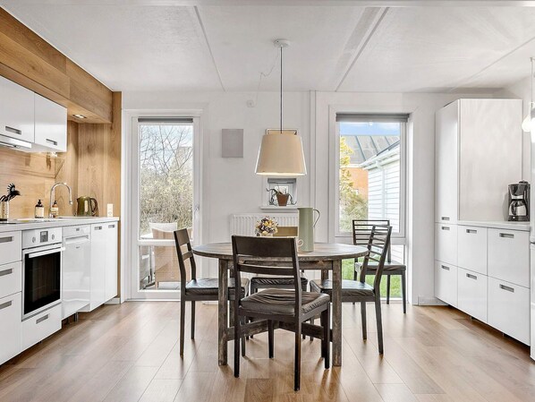 A modern kitchen with white cabinets, a wooden ceiling, and a dining area with a table and chairs.