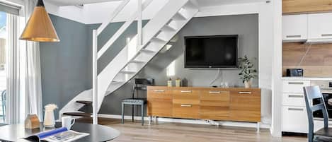 Een moderne woonkamer met een trap, een flatscreen-tv, een houten kast en een eethoek.