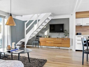 Ett modernt vardagsrum med en trappa, en platt-TV, ett träskåp och en matplats.