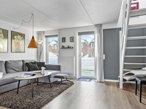A modern living room with a grey sofa, a coffee table, and a lamp. There is a staircase to the right and a door leading outside.