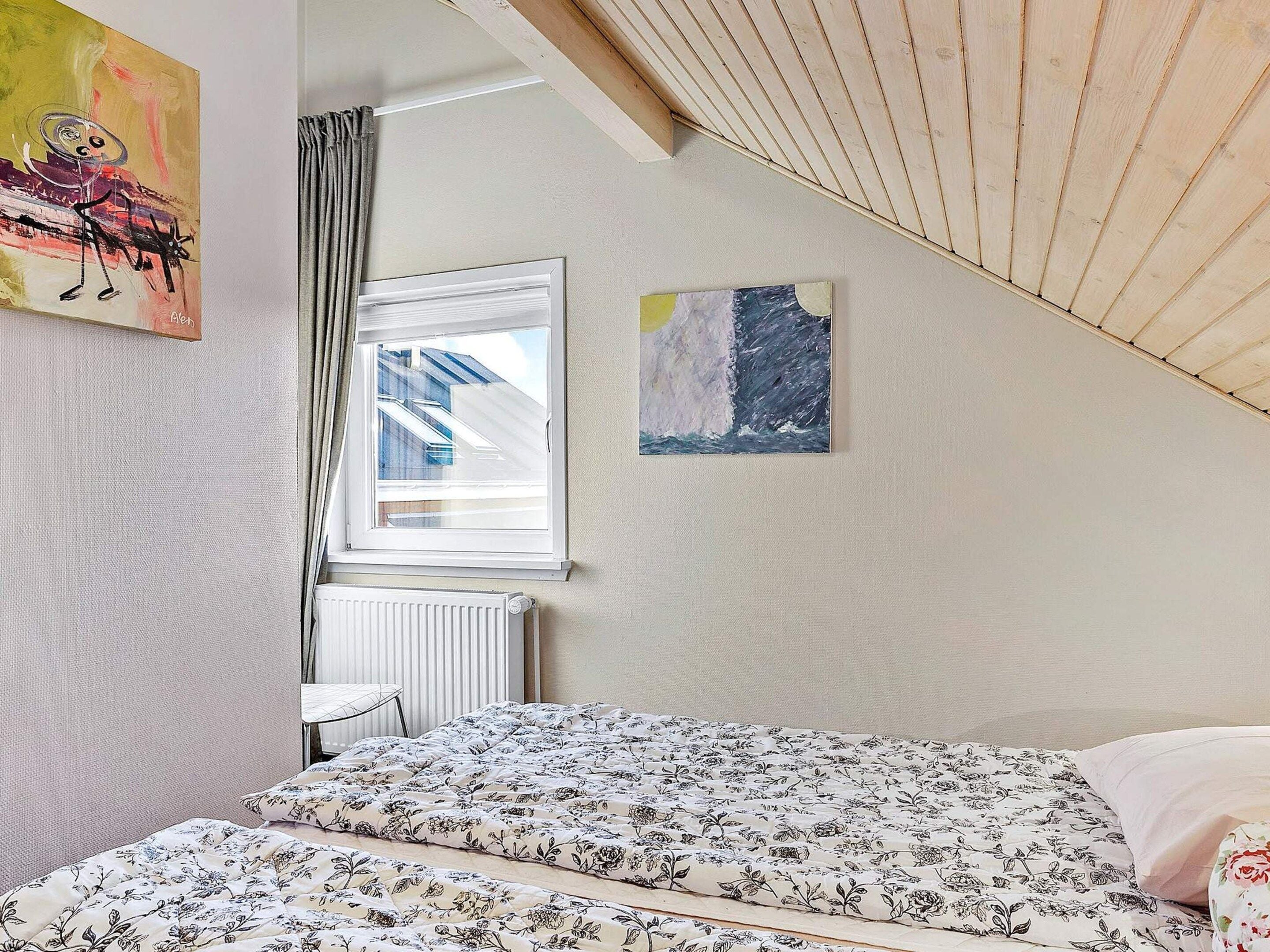 Makuuhuone, jossa on sänky, ikkuna verhoilla, patteri ja kaksi seinälle ripustettua taulua.
