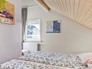 Makuuhuone, jossa on sänky, ikkuna verhoilla, patteri ja kaksi seinälle ripustettua taulua.