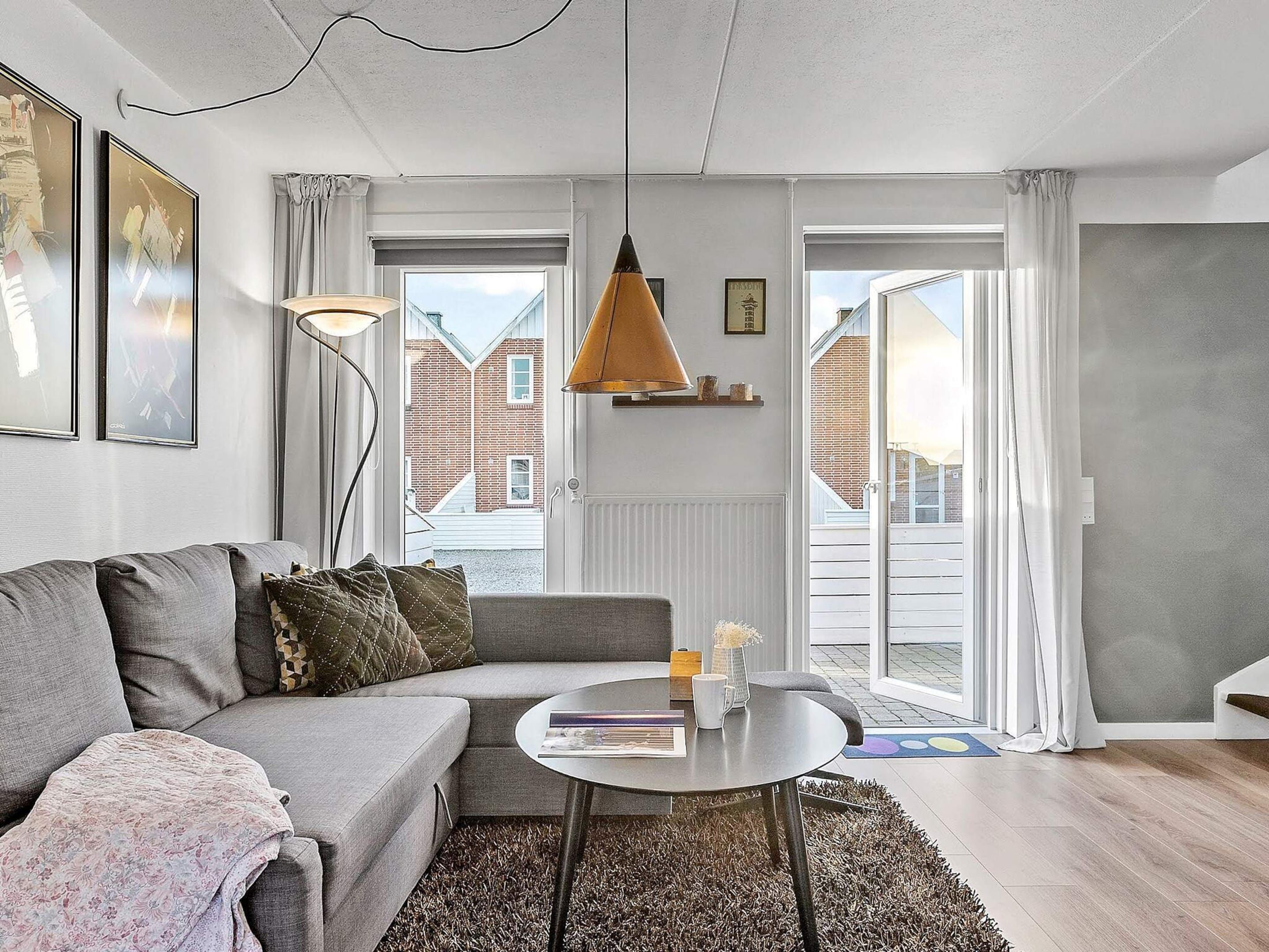 Ein modernes Wohnzimmer mit einem grauen Sofa, einem runden Couchtisch und einer hängenden Pendelleuchte.