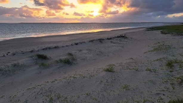 A beach with a sunset, sandy shore, and a clear sky.
