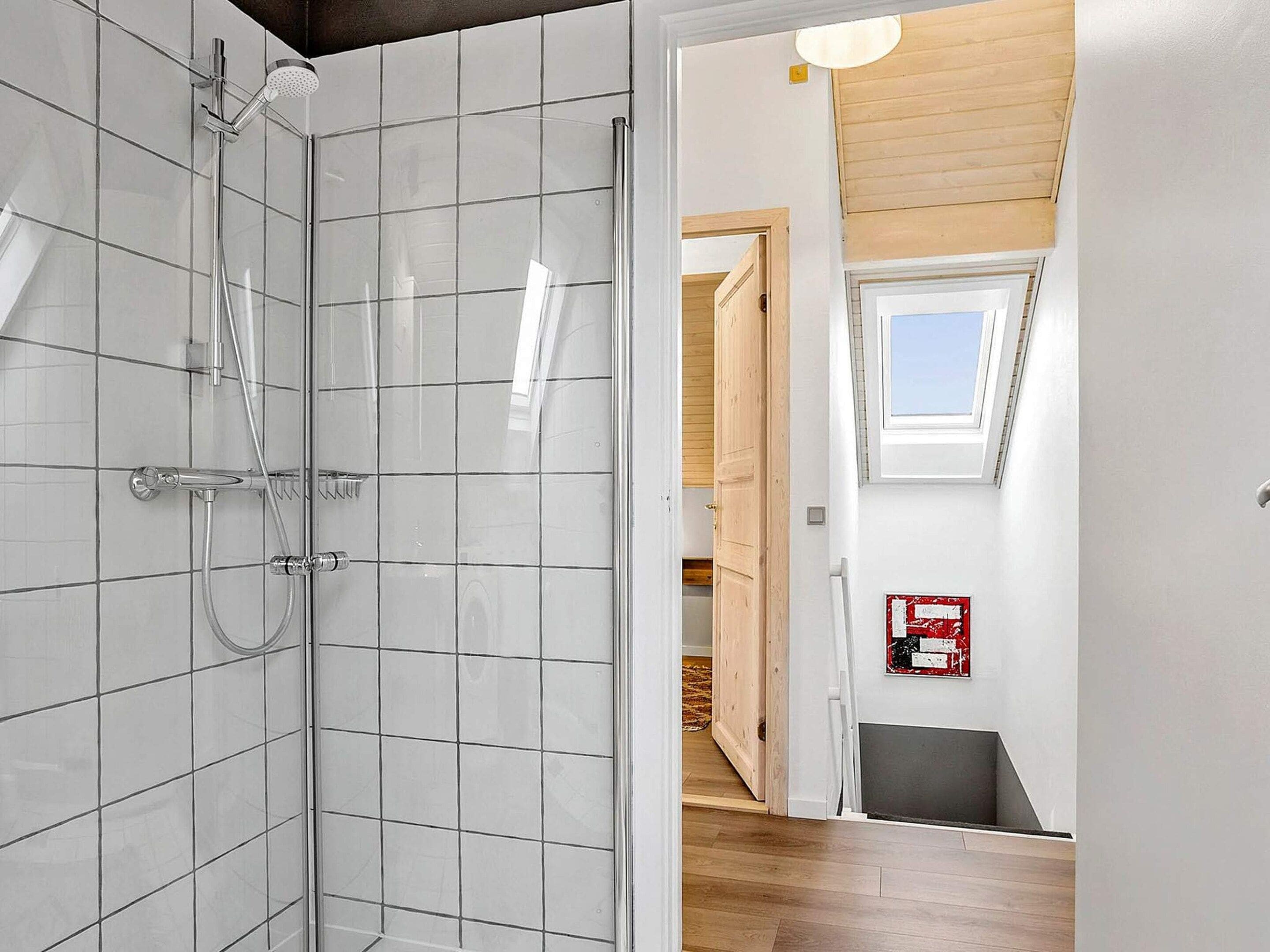 Un bagno moderno con cabina doccia in vetro, una porta ben visibile che dà su un interno in legno e un estintore a parete.