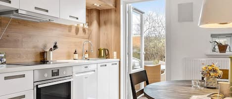 A modern kitchen with white cabinetry, a built-in oven, and a dining area with a round table and chairs.