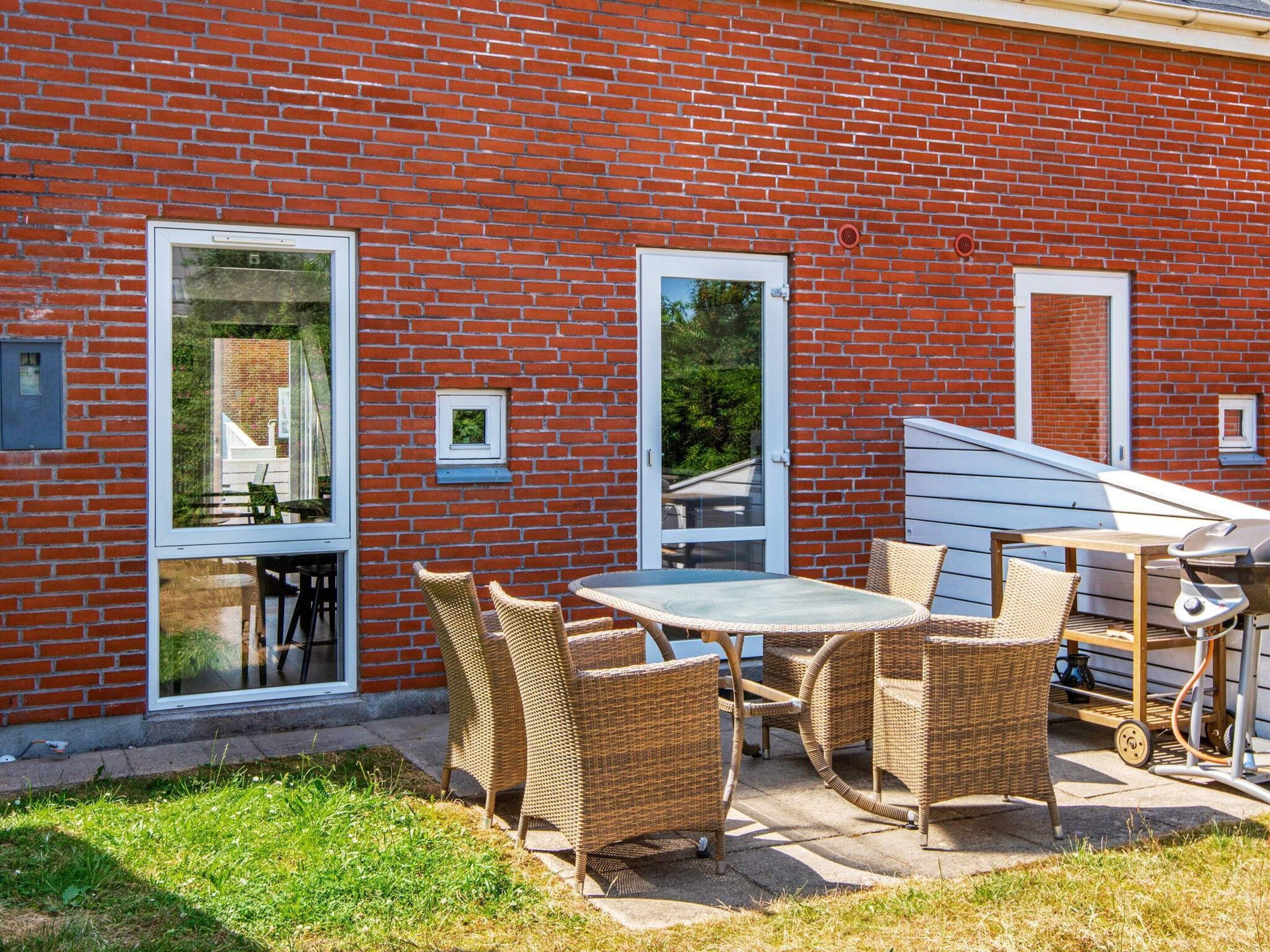 A brick building with a patio area featuring wicker furniture and a grill.