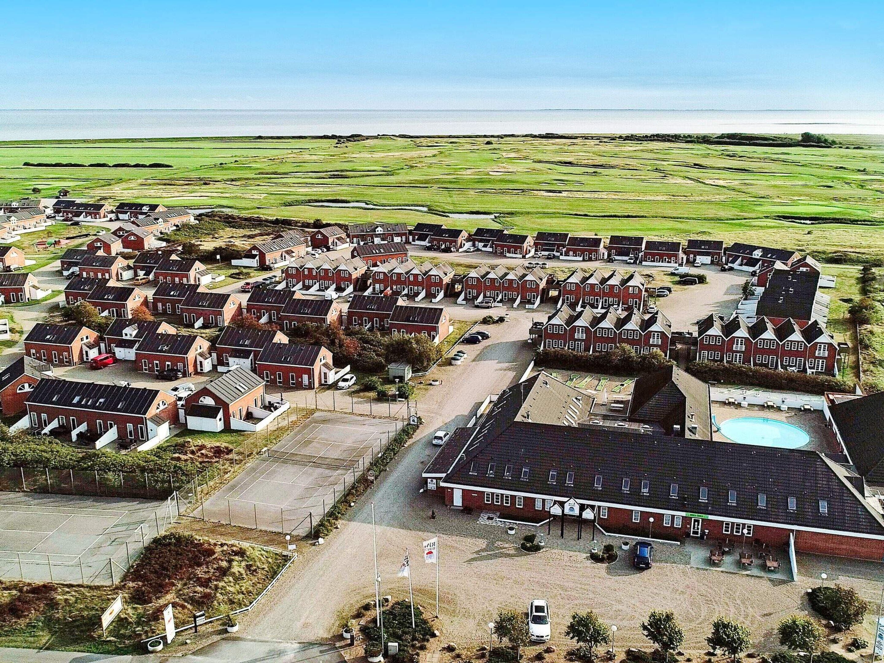 A residential area with multiple red-roofed houses arranged in rows, a large parking area, and a swimming pool.