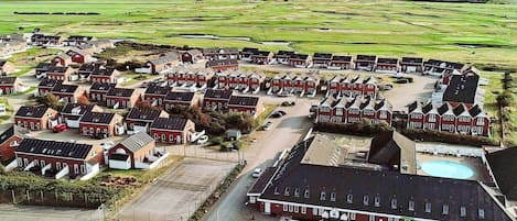 A residential area with multiple red-roofed houses arranged in rows, a large parking area, and a swimming pool.