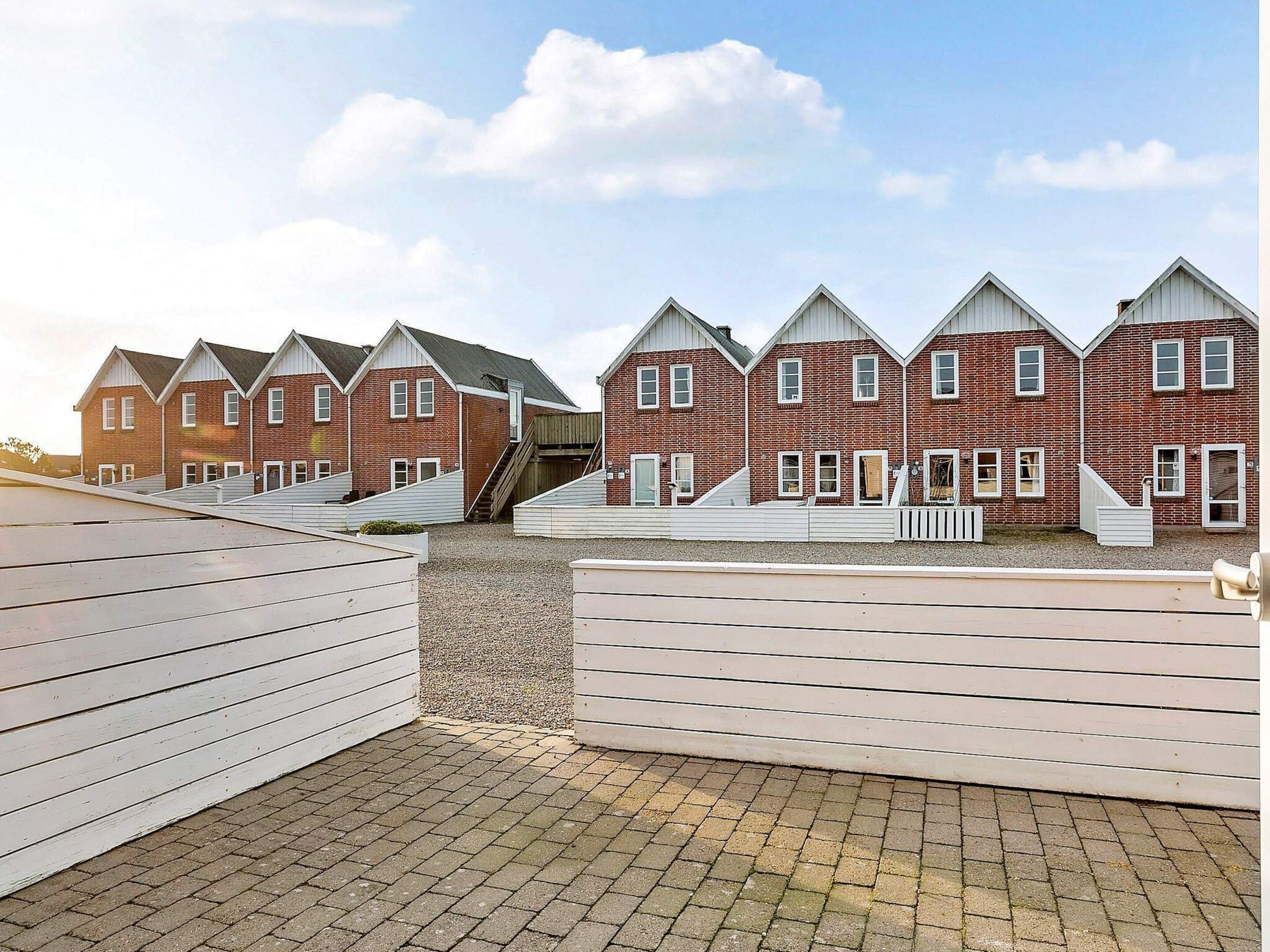 A row of red brick houses with white trim and gabled roofs, arranged in a linear fashion.