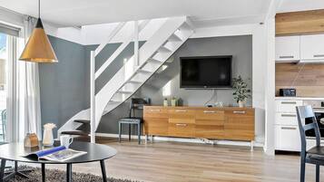 A modern living room with a staircase, a flat-screen TV, wooden cabinets, and a dining area.