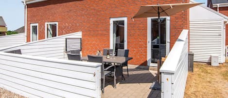 A red brick house with a patio area featuring a table and chairs, a white fence, and a covered outdoor seating area.